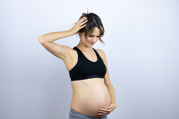 Young sportswoman pregnant wearing sportswear over white background suffering from headache desperate and stressed because pain and migraine with her hands on head