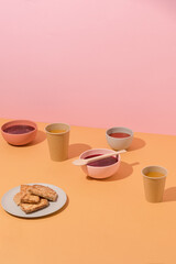Plates with beetroot soup, borscht, pancakes and cups of orange juice on yellow table, abstract composition. Eco dish. Conceptual art, healthy lunch, still life, food photography, copy space