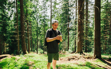 Handsome young man in casual clothes stands in the woods on a summer day with a backpack on his...