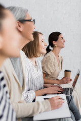 cheerful woman smiling near multicultural group of women during seminar on blurred foreground and...