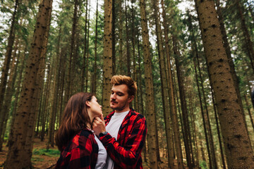 Beautiful couple of man and woman in red shirts hugging in the woods and looking at each other in love. Love story photo.