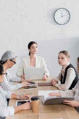 successful team leader looking at businesswomen near multicultural colleagues during meeting