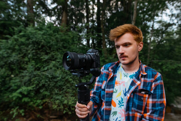 Young man shoots a travel video on camera on a stabilizer with a serious face. Blogger creates video content in nature.