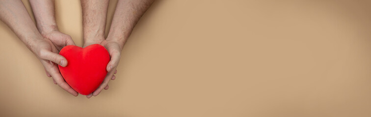 Obraz premium LGBT concept. Horizontal banner with men hands holding red heart on beige background with copy space. Hands of homosexual couple on set sail champagne color. Same sex love. Gay Valentines card