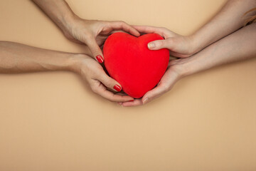 LGBT concept. Women hands holding red heart on beige background with copy space. Hands of homosexual couple on set sail champagne color. Same sex love. Lesbi Valentines card