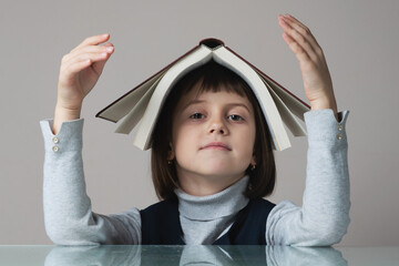 Funny image of happy little school girl holding book on her head.