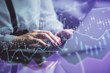 Double exposure of businesswoman hands typing on computer and financial graph hologram drawing....