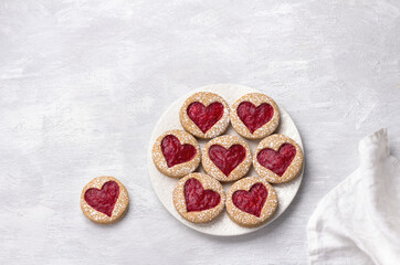 Homemade shortbread spicy cookie with red hearts with jam, on white plate, on gray textured background, for valentine's day. flat lay, space


