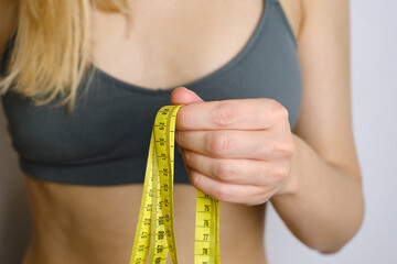 A body centimeter in the hands of girl in tracksuit after a workout or fitness session. Measurement of body volume. Sports waist. Healthy lifestyle, physical activity. Controlling figure while dieting