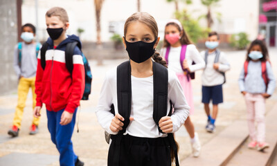 Portrait of tweenager girl in protective mask with backpack going to school lessons on warm autumn day. New lifestyle during coronavirus pandemic.