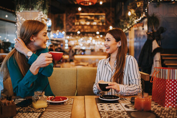 Two best friends sitting in coffee bar or restaurant after shopping and happily talking together.