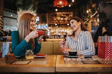 Two best friends sitting in coffee bar or restaurant after shopping and happily talking together.