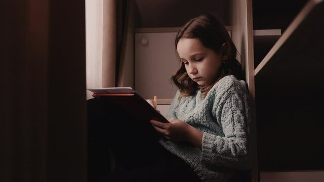 young girl with satin hair in warm sweater writes letter to Santa Claus standing on the bed ladder by the window
