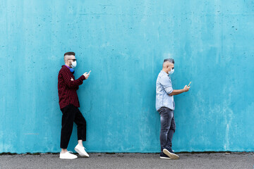 Cool men in a line using mobile phones while keeping social distance and wearing face medical mask...