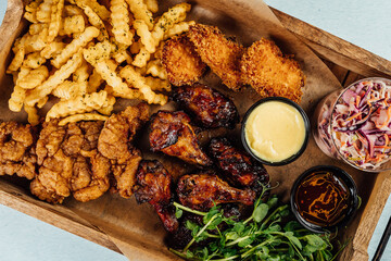 Top view of fried chicken with french fries and sauce on a wooden tray on the table