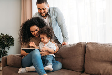 Happy family using digital tablet. Young parents looking how their son learning at home.