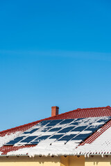 Solar photovoltaic panels PV on a snowy house roof, blue sky with copy space. - 408821606