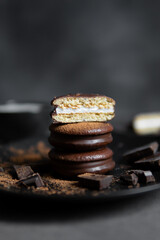 Round chocolate brownie on a black plate and cocoa powder on a gray concrete table. Sweets and coffee background.