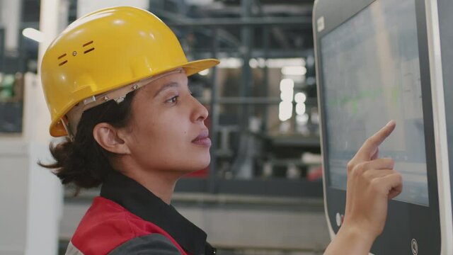 Slow-motion close-up of female mixed race engineer setting parameters for machinery equipment using touchscreen working at factory