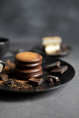 Round chocolate brownie on a black plate and cocoa powder on a gray concrete table. Sweets and coffee background.