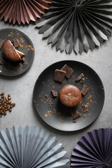 Round chocolate brownie on a black plate and cocoa powder on a gray concrete table. Sweets and coffee background. view from above. flat lay