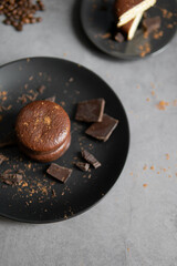 Round chocolate brownie on a black plate and cocoa powder on a gray concrete table. Sweets and coffee background.