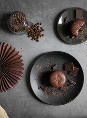 Round chocolate brownie on a black plate and cocoa powder on a gray concrete table. Sweets and coffee background. view from above. flat lay