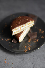 Round chocolate brownie on a black plate and cocoa powder on a gray concrete table. Sweets and coffee background.
