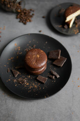 Round chocolate brownie on a black plate and cocoa powder on a gray concrete table. Sweets and coffee background.