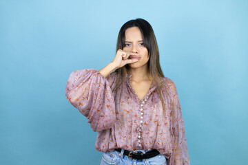 Beautiful latin woman wearing a pink shirt over blue isolated background mouth and lips shut as zip...