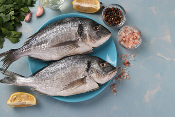 Two raw fish dorado with spice and lemon on blue plate on light blue background. Top view