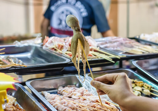 Close up of raw squid with hand woman holding on skewers fresh dollfus' octopus at market. Selective focus on Fresh squids octopus or cuttlefish for cooked food at restaurant or seafood market