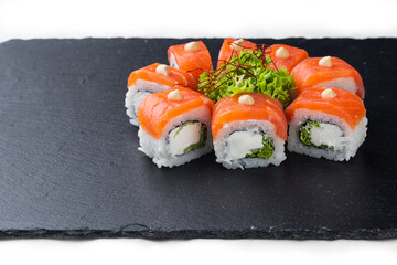 Sushi roll with salmon, avocado and cheese on a black stone plate on a white plate. Sushi menu. Japanese food.