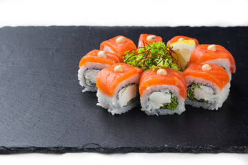 Sushi roll with salmon, avocado and cheese on a black stone plate on a white plate. Sushi menu. Japanese food.