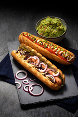 Gourmet dirty hot dog sandwich with various garnish on black slate background. Healthy option of...