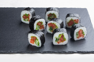 Sushi roll with salmon, avocado and cheese on a black stone plate on a white plate. Sushi menu. Japanese food.