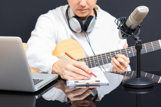 Young Asian Male Songwriter Writing A Hit Song While Playing Acoustic Guitar. Songwriting Concept