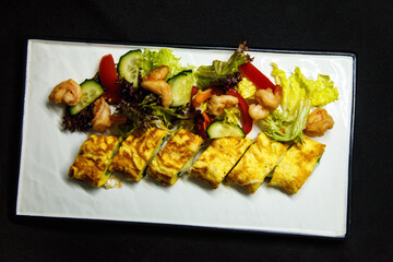 Roll of omelette and fresh salad on a black background