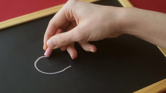 Girl's hand draws pink chalk heart fnd love on blackboard