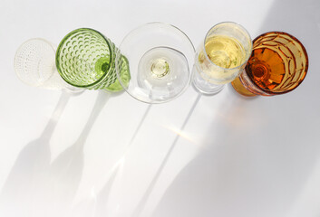 Line of Transparent and green and vintage yellow wine glasses and their sun created shadows on clean white background. Minimal celebration concept. Wine testing.