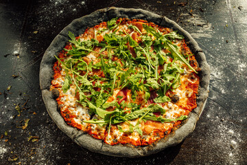 A top view of appetizing pizza with black dough and various vegetables