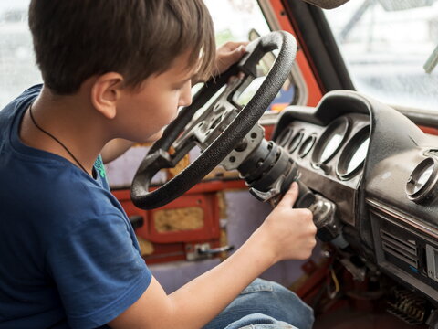 An 11-year-old boy enthusiastically plays the driver behind the wheel of an old abandoned car.