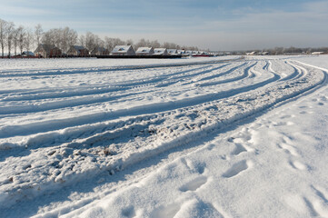 Fototapeta na wymiar Winter. Sunny and frosty day. The outskirts of the village and car tracks in the snow