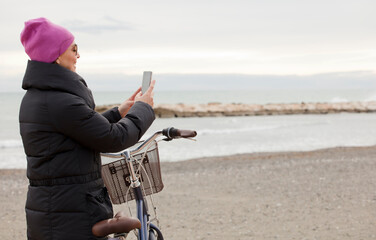 Elegant woman with bicycle and using a cellphone. Near the sea, space for text