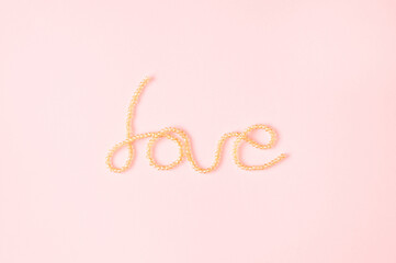 Word love written with shiny pearls on a light pink background. Minimal photography