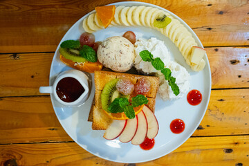 Ice cream on toast with whipped cream, banana slices, strawberry juice and honey in a cup