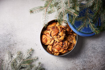 Freshly made Swedish swirl buns with cinnamon, sprinkled with pearled sugar, in tin cookie box with lid open. Shot on light background, with fir tree branches slightly overlapping the box