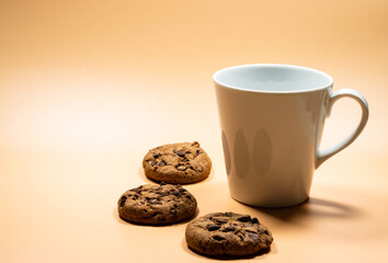 Close up white mug of milk and pile of dark chocolate chip cookies