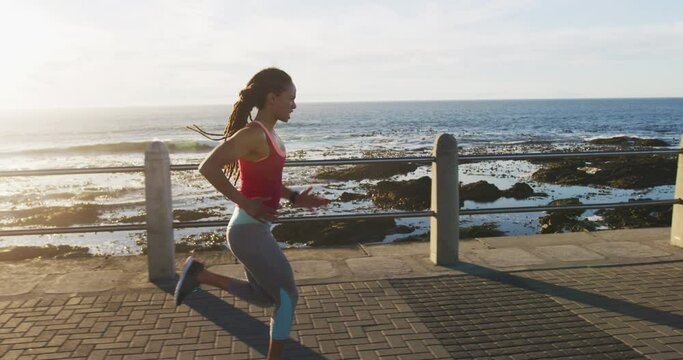 African american woman in sportswear running on promenade by the sea