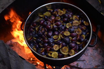 cooking plum jam in a traditional style with firewood. boiling the fruit outside in a large...